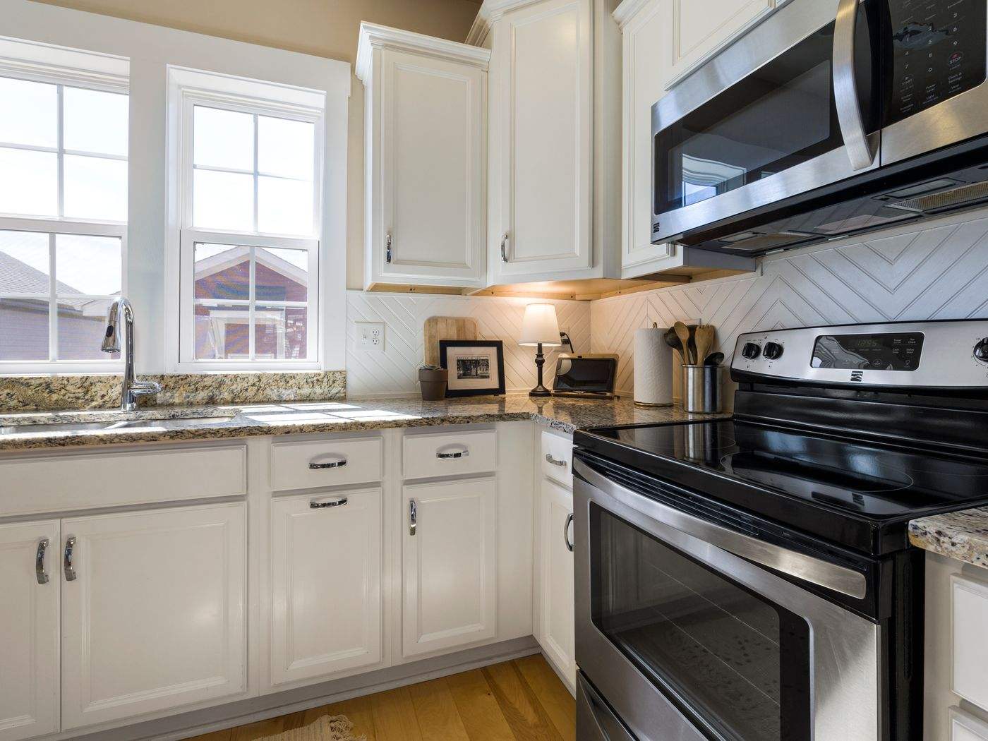 Cabinet painting Boston MA: bright kitchen with white painted cabinets, granite countertops and stainless steel appliances